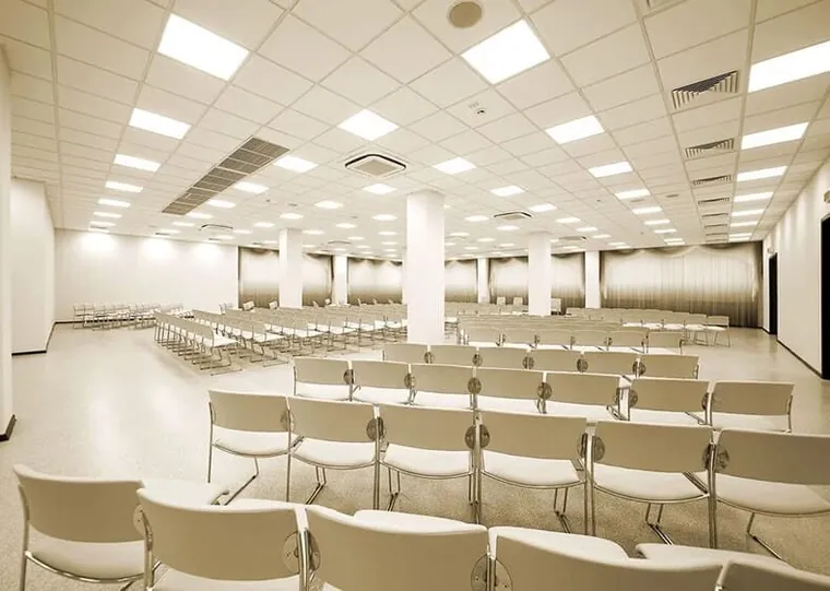 Auditório com cadeiras alinhadas sob forro modular branco com luminárias embutidas