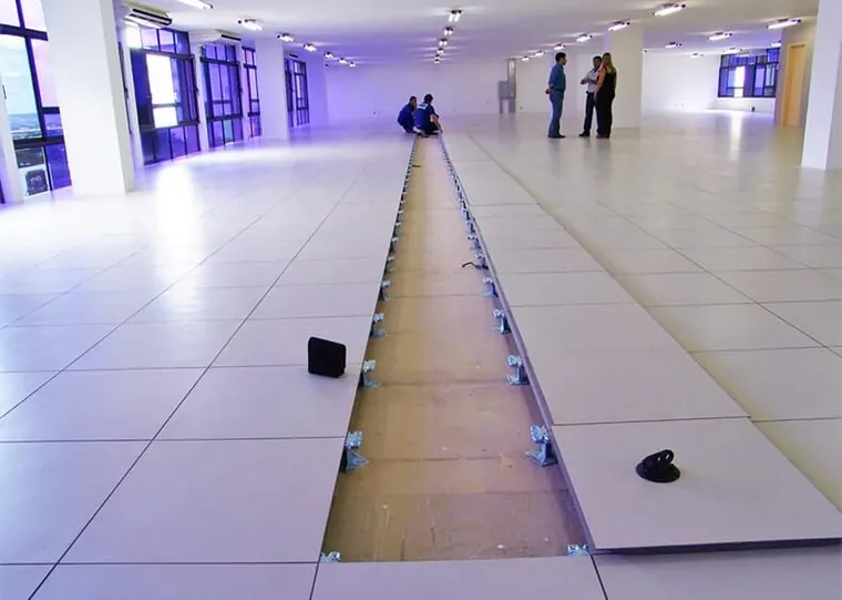 Piso elevado sendo montado num corredor amplo, com as placas abertas e os pedestais à vista